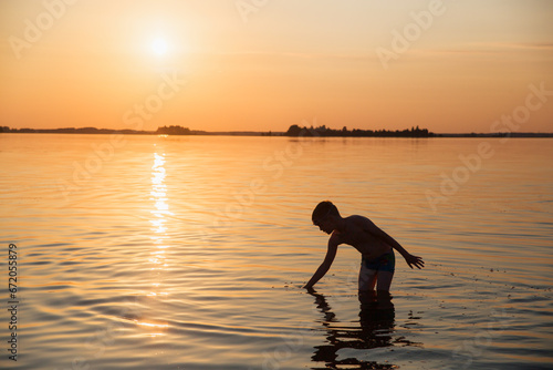 Silhouette of a child playing in the water against the backdrop of a beautiful sea sunset.