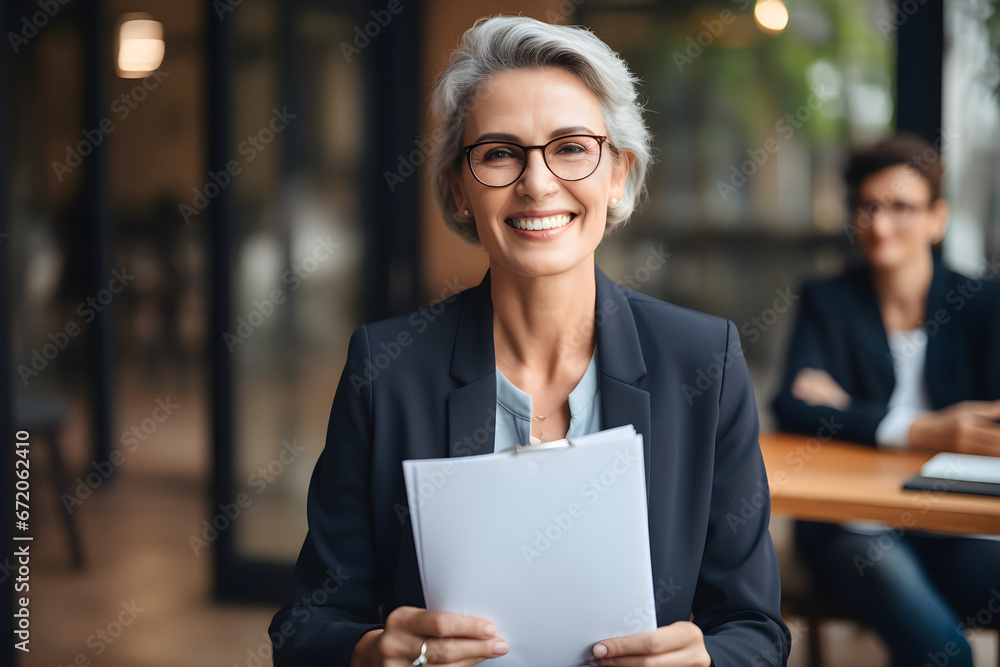 Smiling mature business woman hr holding cv at job interview. Happy mid aged professional banking financial manager, insurance agent, lawyer consulting clients sitting at work corporate office meeting