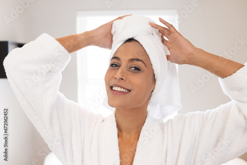 Portrait of happy biracial woman wearing white bathrobe and towel on head in bathroom photo