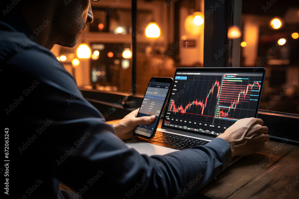 Investor using mobile phone and laptop checking trade market data. Stock trader broker looking at computer analysing trading crypto currency finance market crypto stock market data, over shoulder view - obrazy, fototapety, plakaty 