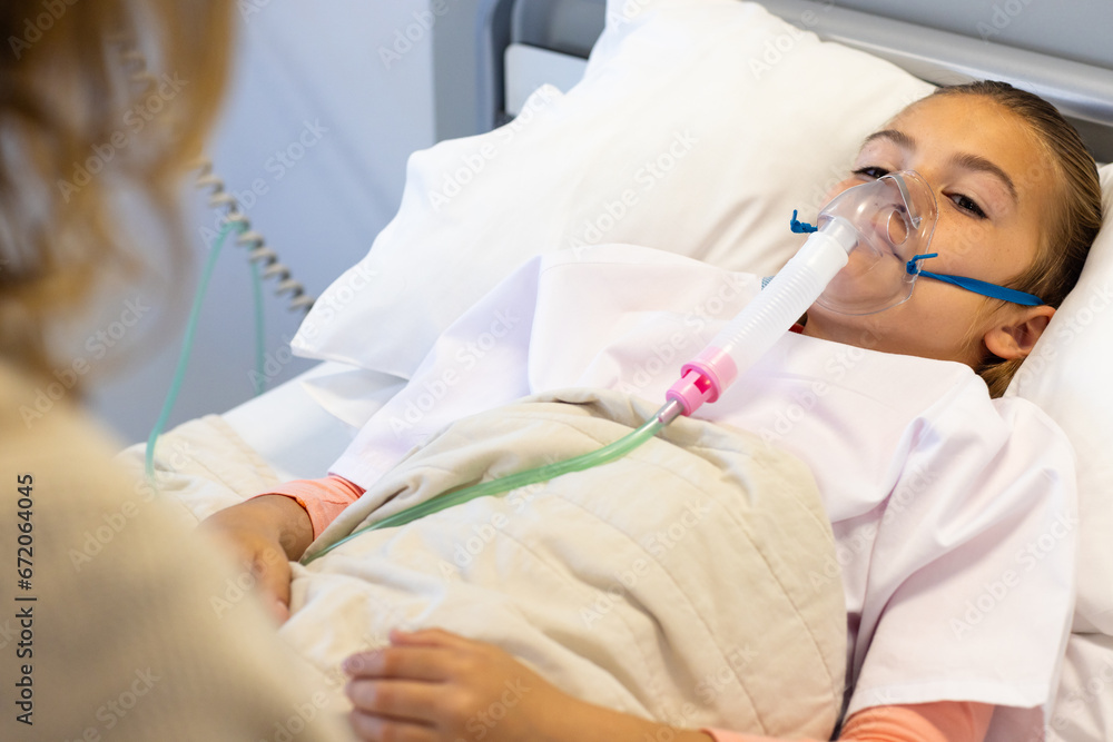 Caucasian mother sitting with daughter patient in oxygen mask lying in hospital bed Caucasian mother sitting with daughter patient in oxygen mask lying in hospital bed
