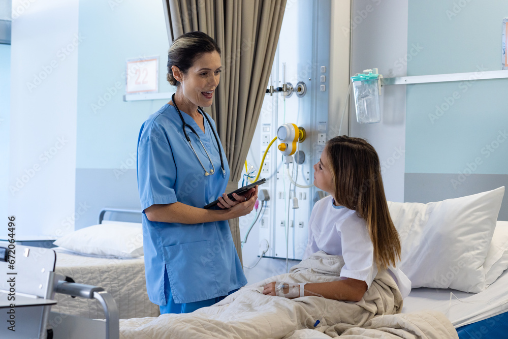 Smiling caucasian female doctor with tablet and girl patient in hospital bed talking Smiling caucasian female doctor with tablet and girl patient in hospital bed talking