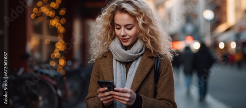 At the background of the city street a stunning beautiful young woman with blonde hair can be seen messaging on her smart phone She is a pretty girl engaged in a conversation on her mobile d photo