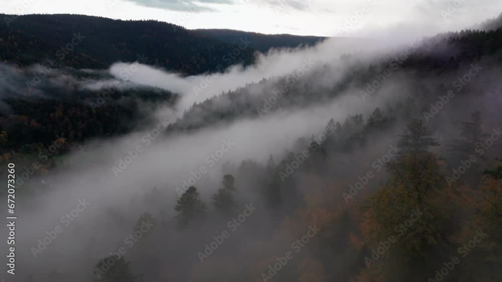 Aerial view flying above thick clouds over mystical automnal mountain forest, 4K