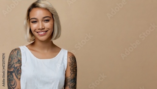 Smiling blond pretty smiling girl beauty female gen z model with short blonde hair beautiful face healthy skin and tattoo looking at camera wearing white top isolated at beige background