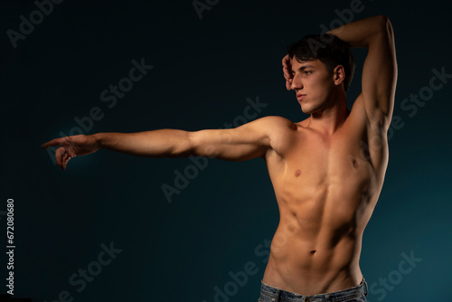 young athletic guy posing with uotstretched hand. concept: the male body after exercise and diet. men's health. Blue studio background