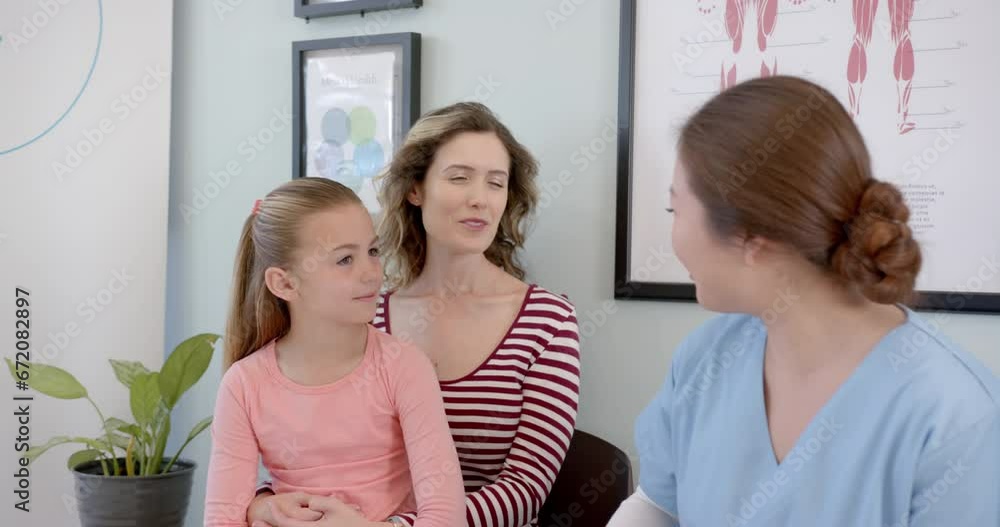 Happy diverse girl patient sitting with mother and female nurse talking in hospital, slow motion Happy diverse girl patient sitting with mother and female nurse talking in hospital, slow motion