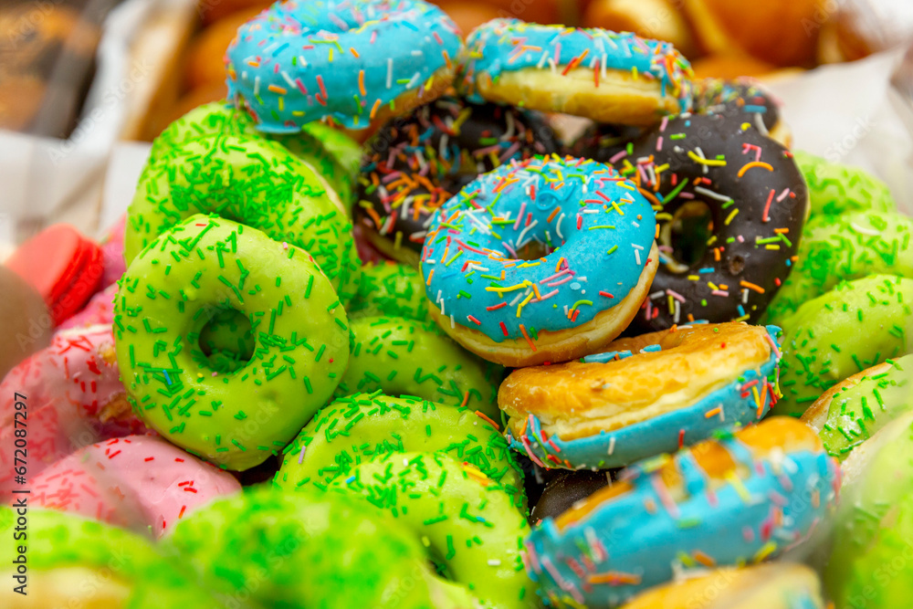 Many donuts with multi-colored glaze on the counter in a store. Delicious baked goods. Close-up.
