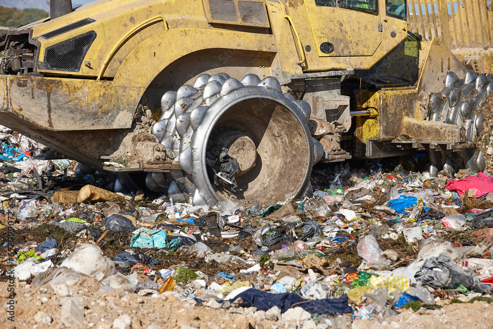 Fototapeta premium Heavy machinery shredding garbage in an open air landfill. Pollution management