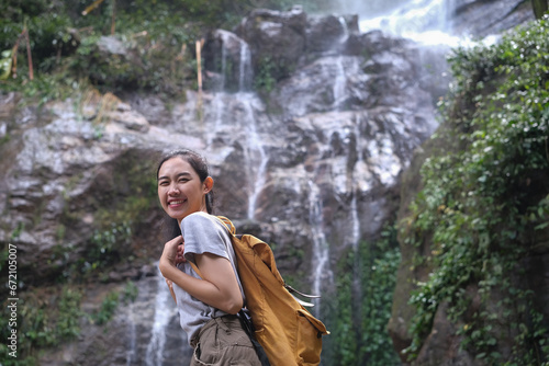 Portrait of smiling female adventurous with backpack standing in front of tropical waterfall