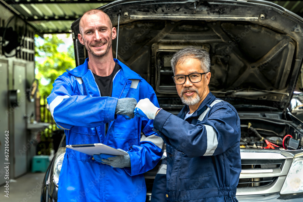 Young Caucasian car mechanic man doing bump fist hands with senior technician during working in car repair shop Young Caucasian car mechanic man doing bump fist hands with senior technician during working in car repair shop