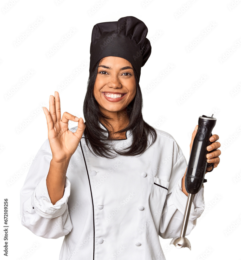 Young Filipina chef with hat holding a mixer cheerful and confident showing ok gesture. Young Filipina chef with hat holding a mixer cheerful and confident showing ok gesture.