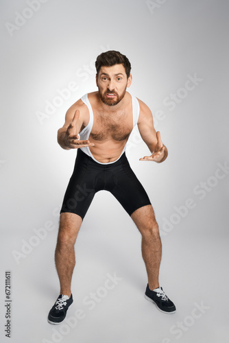 Angry wrestler in black and white singlet getting ready to attack, while looking at camera. Front view of male athlete grimacing, while staying in wrestling stance, isolated on white. Sport concept.