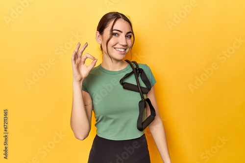 Fitness young woman with resistance bands cheerful and confident showing ok gesture.