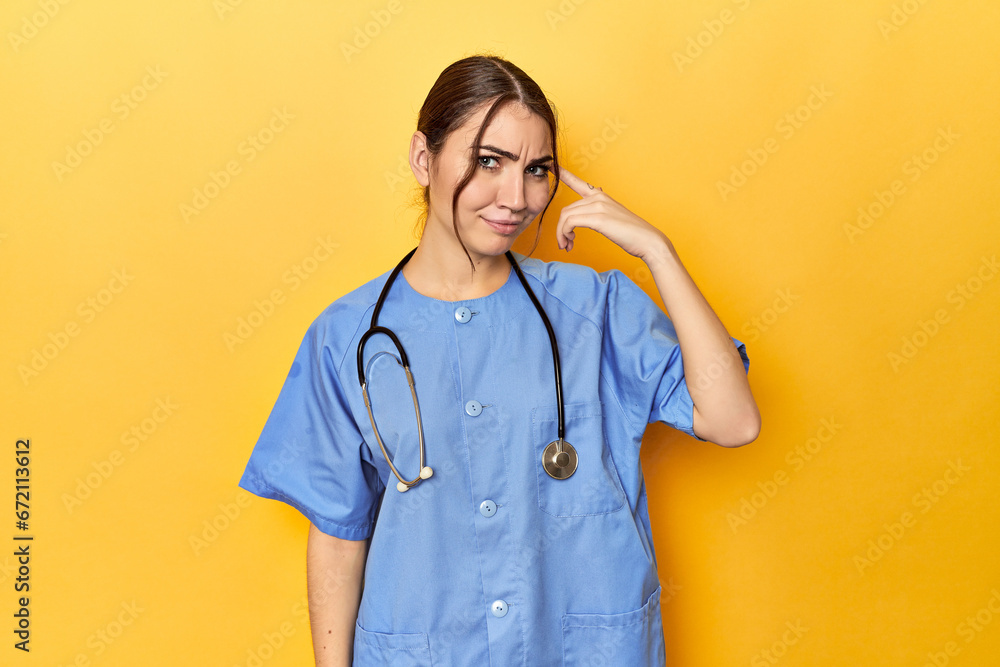 Young nurse in a yellow studio showing a disappointment gesture with forefinger.