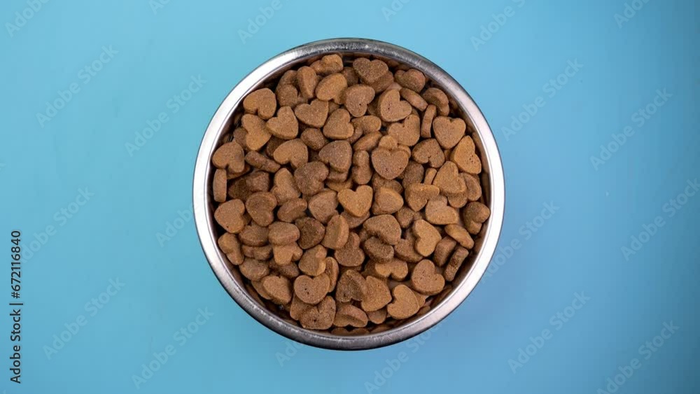 Dog bowl filled with heart-shaped kibble rotates against a sky-blue backdrop. Animal love concept. Dog bowl filled with heart-shaped kibble rotates against a sky-blue backdrop. Animal love concept.