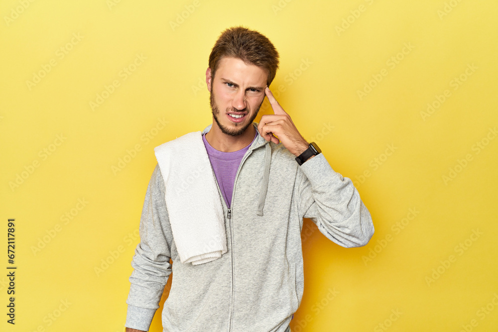 Sporty man in sweatshirt and towel on yellow showing a disappointment gesture with forefinger.