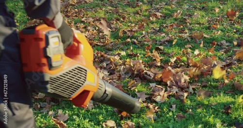 Close up of caucasian concierge in working uniform removing dry fall leaves at city park with hand blower. Concept of people, landscaping and maintaining.