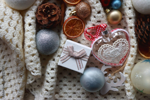 Various colorful Christmas ornaments, small presents and seasonal spices on white knitted blanket. Top view.