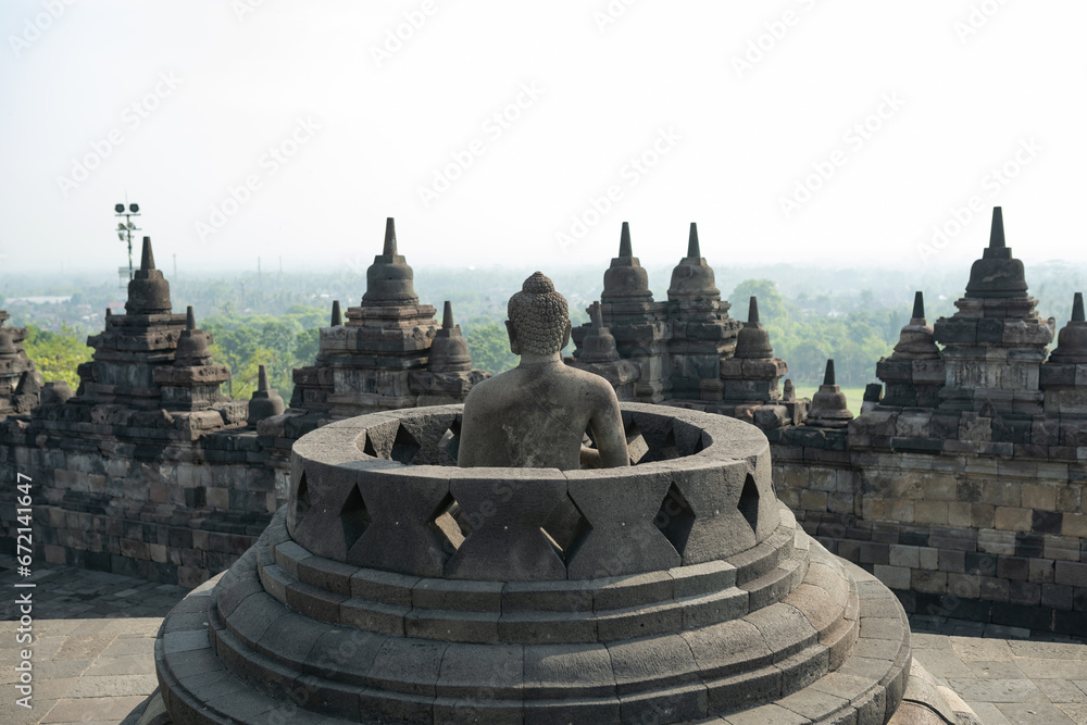 (Selective focus) Stunning view of a Buddha Statue in the foreground and some bell shaped stupas in the background. Borobudur is a Mahayana Buddhist temple in Indonesia.