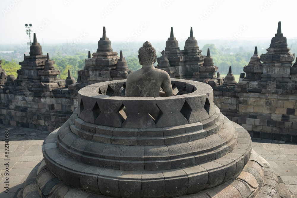 (Selective focus) Stunning view of a Buddha Statue in the foreground and some bell shaped stupas in the background. Borobudur is a Mahayana Buddhist temple in Indonesia.