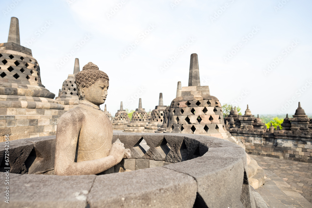 (Selective focus) Stunning view of a Buddha Statue in the foreground and some bell shaped stupas in the background. Borobudur is a Mahayana Buddhist temple in Indonesia.