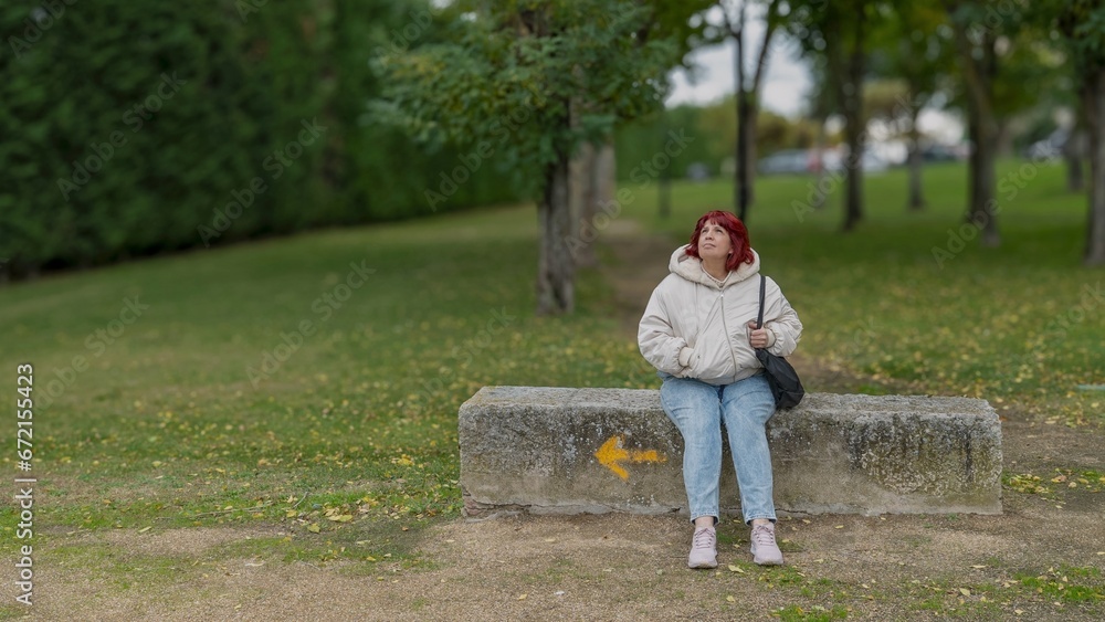 Fototapeta premium Woman in her 60s sitting on a bench outside looking at the sky and thinking. Arrow pointing the way.