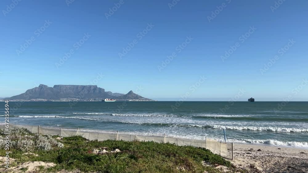 Beach waves white sand with views of Table Mountain and ships out at sea in Table Bay Cape Town on a sunny day Beach waves white sand with views of Table Mountain and ships out at sea in Table Bay Cape Town on a sunny day