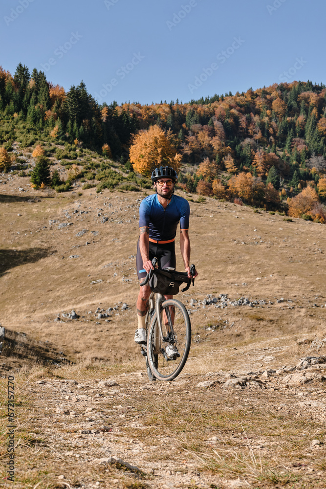 Male cyclist riding a gravel bike during sunny day in autumn mountains. Amazing autumn foliage. Cycling in the nature. Adventure cycling concept. Man cyclist practicing on gravel road. 