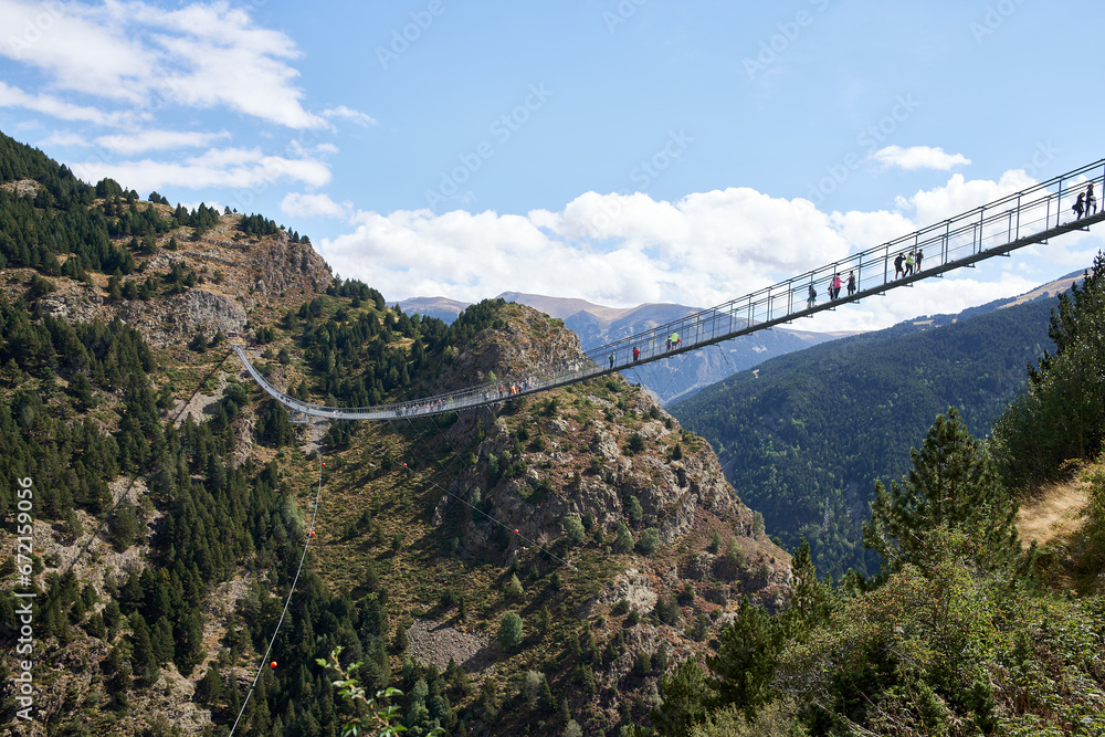 Aerial view of a Tibetan bridge with people crossing surrounded by nature with blue sky with clouds