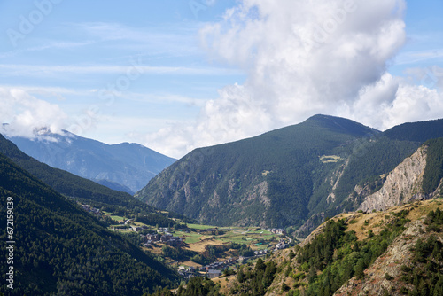 View of a valley with small houses surrounded by large green mountains with blue sky with clouds