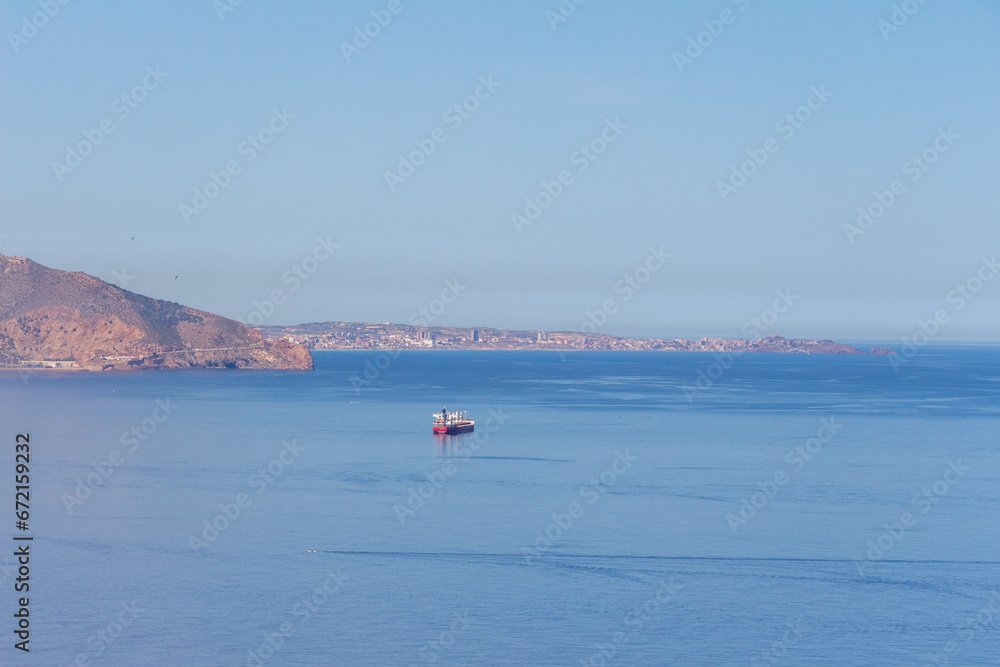 Minimalist blue panorama of the bay of Oran, Algeria. Blue sky, blue sea, a unique cargo boat.