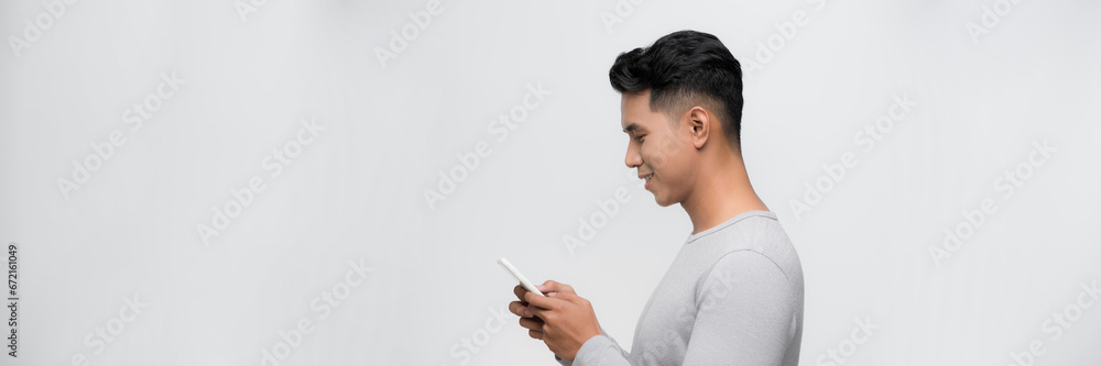 Handsome young man using his phone with smile while standing against white background. Handsome young man using his phone with smile while standing against white background.