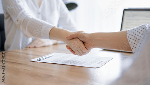 Business people shaking hands above contract papers just signed on the wooden table, close up. Lawyers at meeting. Teamwork, partnership, success concept photo
