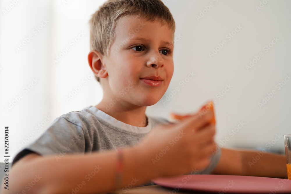 Side view of little boy sitting at table and eating delicious food at home Side view of little boy sitting at table and eating delicious food at home