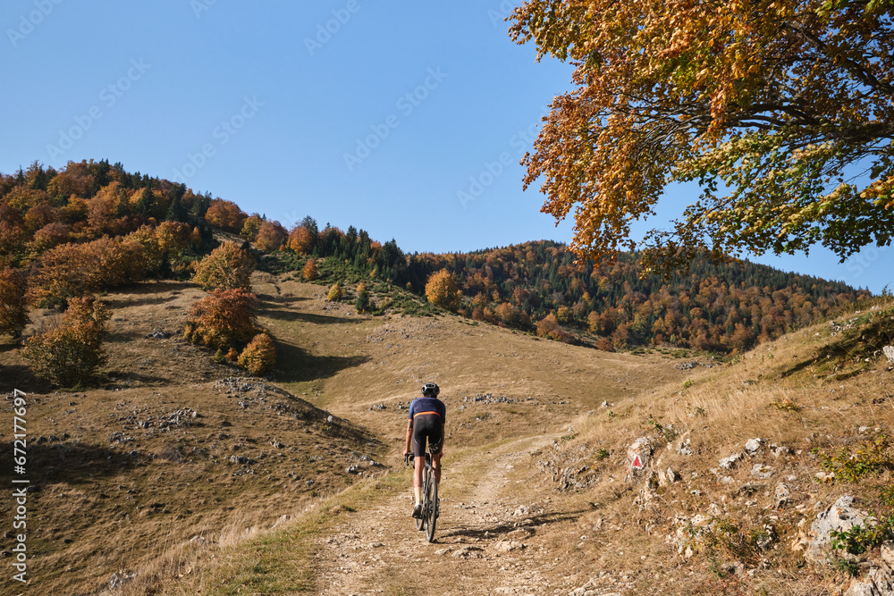 Male cyclist riding a gravel bike during sunny day in autumn mountains. Amazing autumn foliage. Cycling in the nature. Adventure cycling concept. Man cyclist practicing on gravel road. 
