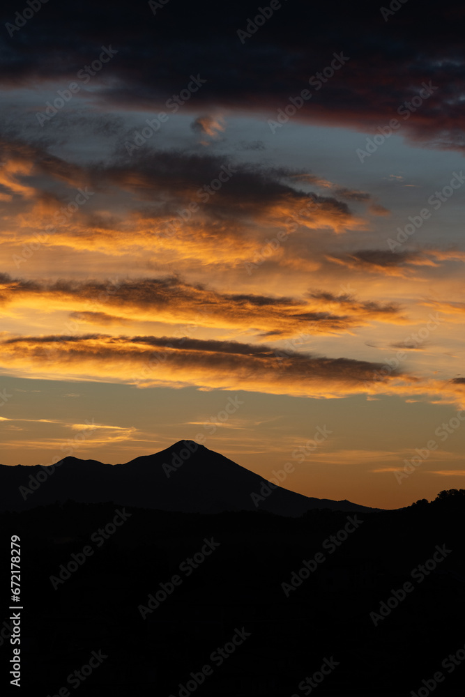 Stunning sunrise with beautiful shades of orange, pink, purple and blue colors with the silhouette of a mountain range. Wallpaper, natural background with copy space.