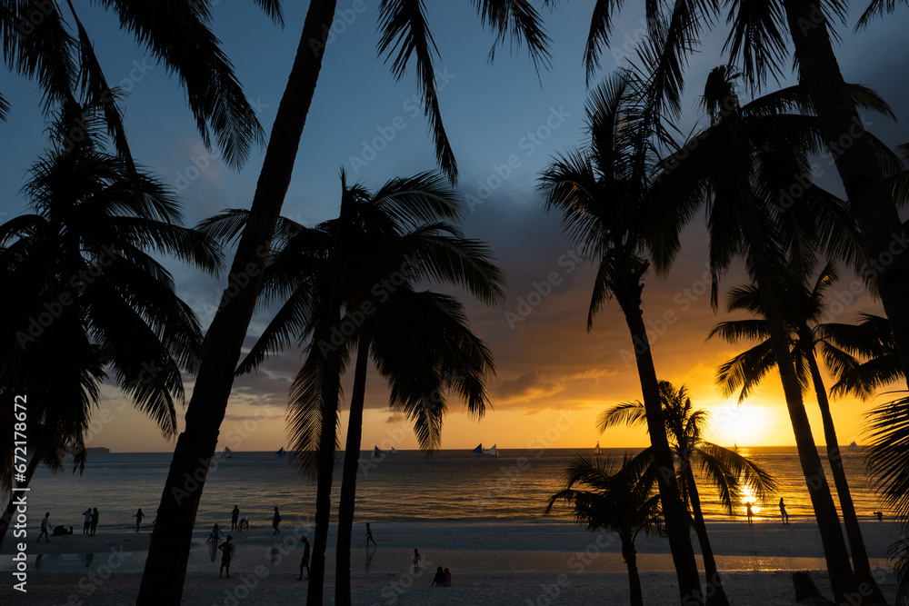 (Selective focus) Stunning view of a dramatic sunset in the background and the silhouette of coconut palm trees in the foreground. White Beach, Boracay Island, Philippines.