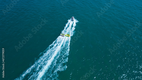 Aerial drone of extreme inflatable towable tube cruising in high speed attached on powerboat with children on sofa ride, watersport