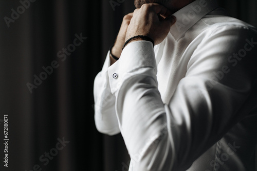 Close up cropped picture of caucasian male adjusting collar of a white shirt. Groom preparing for wedding.