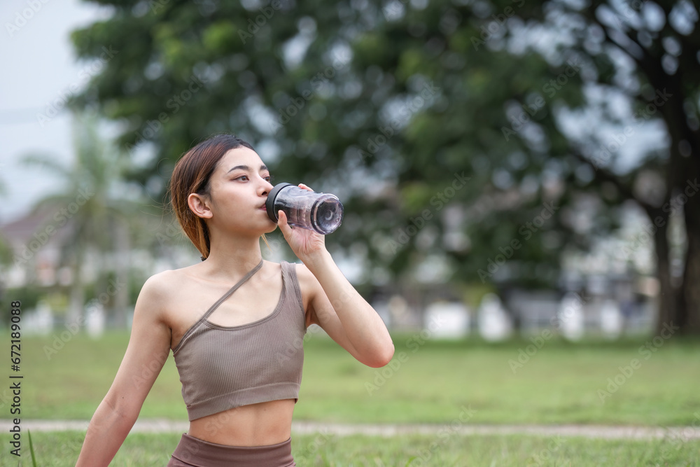 Beautiful young woman drink water after doing yoga in the village park. Yoga or fitness training health care concept