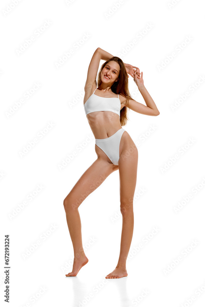 Full length portrait of Slim Caucasian 20s lady posing in white under wear with hands raised up, showing her ideal curves. Full length portrait of Slim Caucasian 20s lady posing in white under wear with hands raised up, showing her ideal curves.
