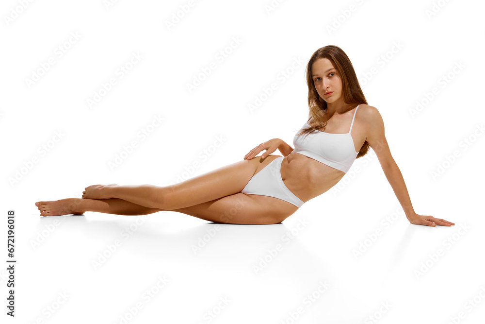 Young beautiful tender fit girl with long hair posing in underwear posing sitting on floor isolated white studio background. Young beautiful tender fit girl with long hair posing in underwear posing sitting on floor isolated white studio background.