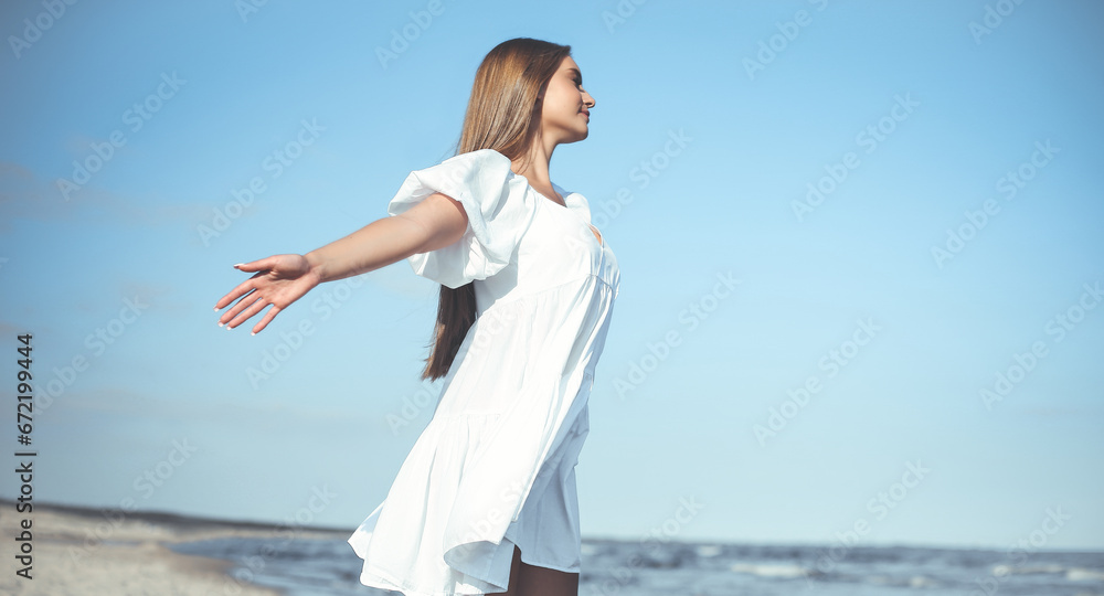 Happy, beautiful woman on the ocean beach standing in a white summer dress, open arms Happy, beautiful woman on the ocean beach standing in a white summer dress, open arms