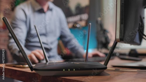 Router stands on the table and distributes Wi-Fi and the man uses this Internet and works at the computer and communicates on his mobile phone