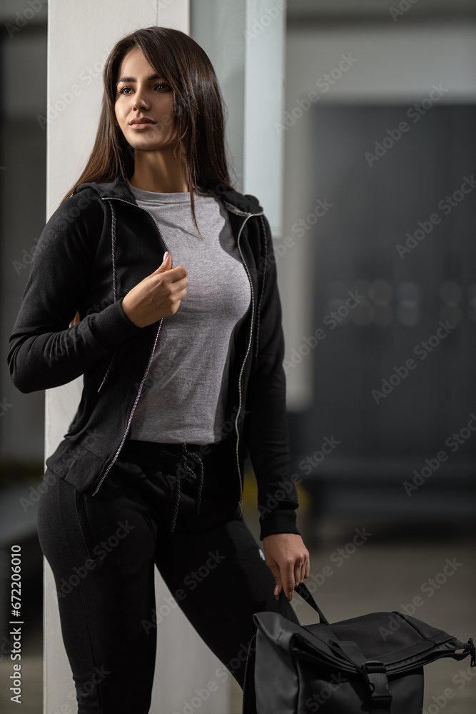 Beautiful fit brunette girl in a black tracksuit holding a sports backpack