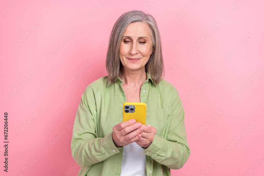 Photo of pensioner woman blogging wearing khaki shirt holding smartphone learning new device instruction isolated on pink color background Photo of pensioner woman blogging wearing khaki shirt holding smartphone learning new device instruction isolated on pink color background