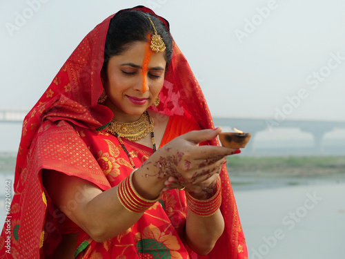 Indian woman holding an earthen lamp in her hand - faith of God  red saree  offering prayers to sun. Hindu woman with handmade clay lamp - Chhath Puja  Bihari festival  Hindu festival  newly wed wo... photo