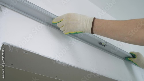 Wallpaper Mural Worker checks the evenness of a white wall with a long building level. Leveling the surface. Torontodigital.ca