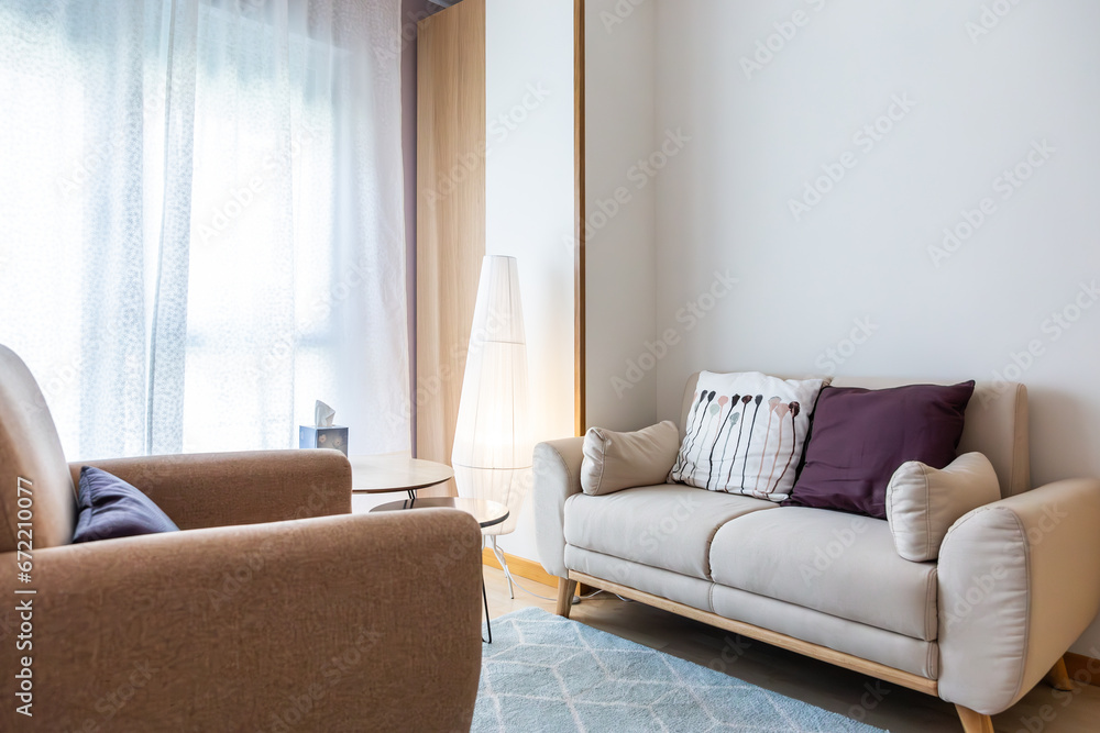 Fototapeta premium Living room with armchairs, cushions, small round tables, floor lamp and a large window with curtain and natural light. Concept of minimalism and simplicity. Copy space